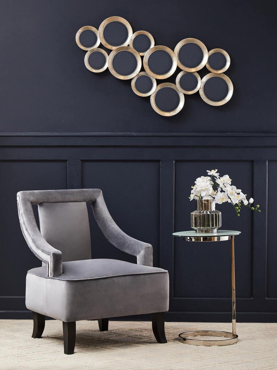 Grey velvet accent chair with mirrored side table and gold circle wall art in modern living room