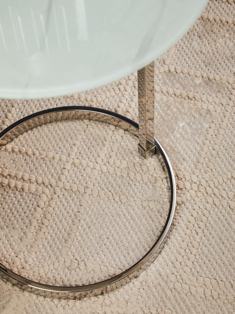 Round glass top side table with chrome metal frame on textured beige rug