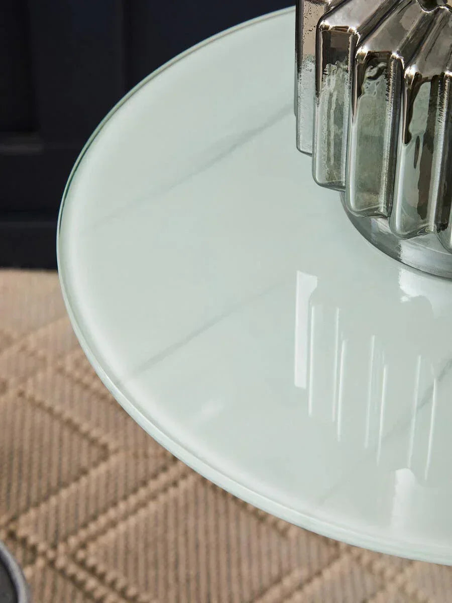 Round glass side table top with silver ceramic vase on beige patterned rug