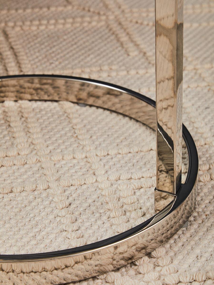 Chrome metal table leg with circular base on textured cream rug
