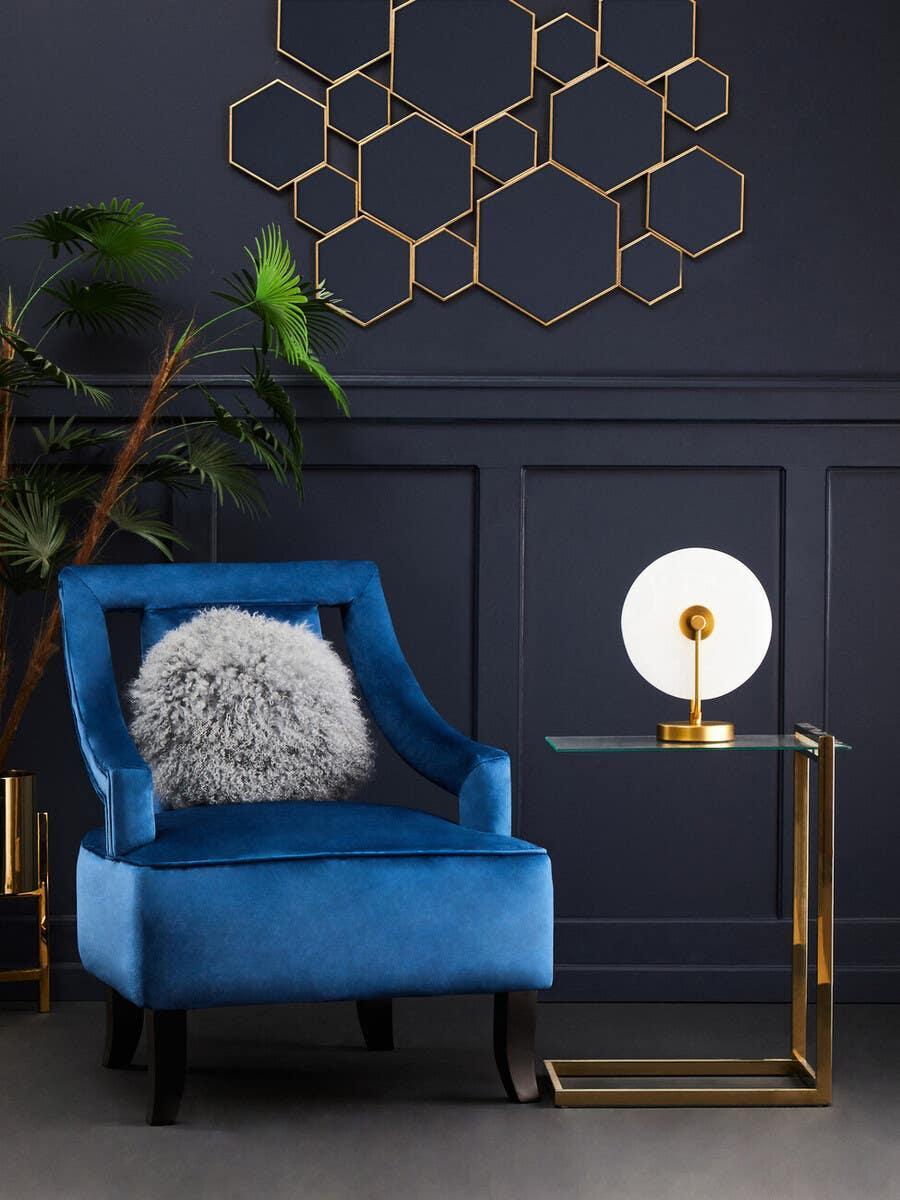 Blue velvet accent chair with grey cushion beside modern glass side table and gold wall art