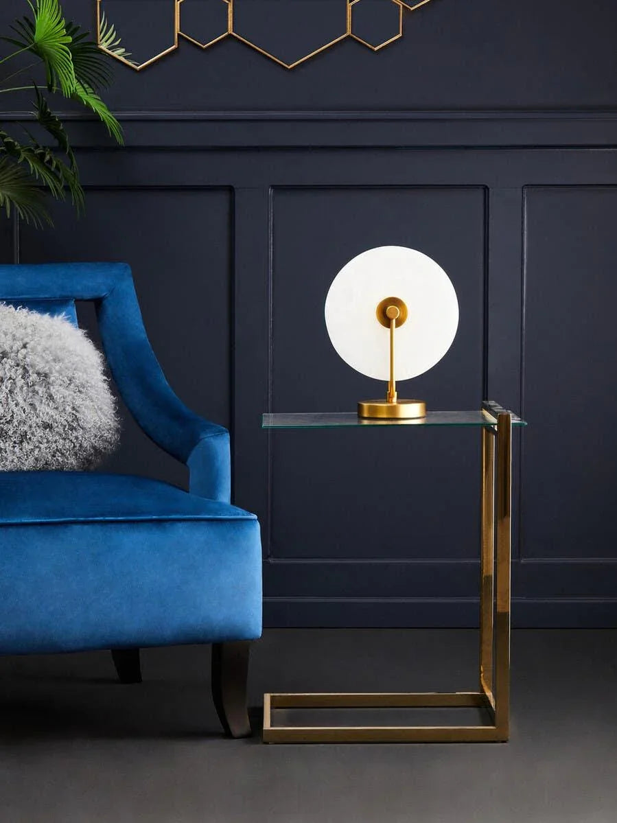 Modern glass side table with gold metal frame beside blue velvet armchair in living room