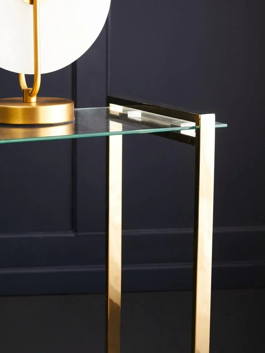 Glass side table with gold metal legs and modern lamp on top against navy wall