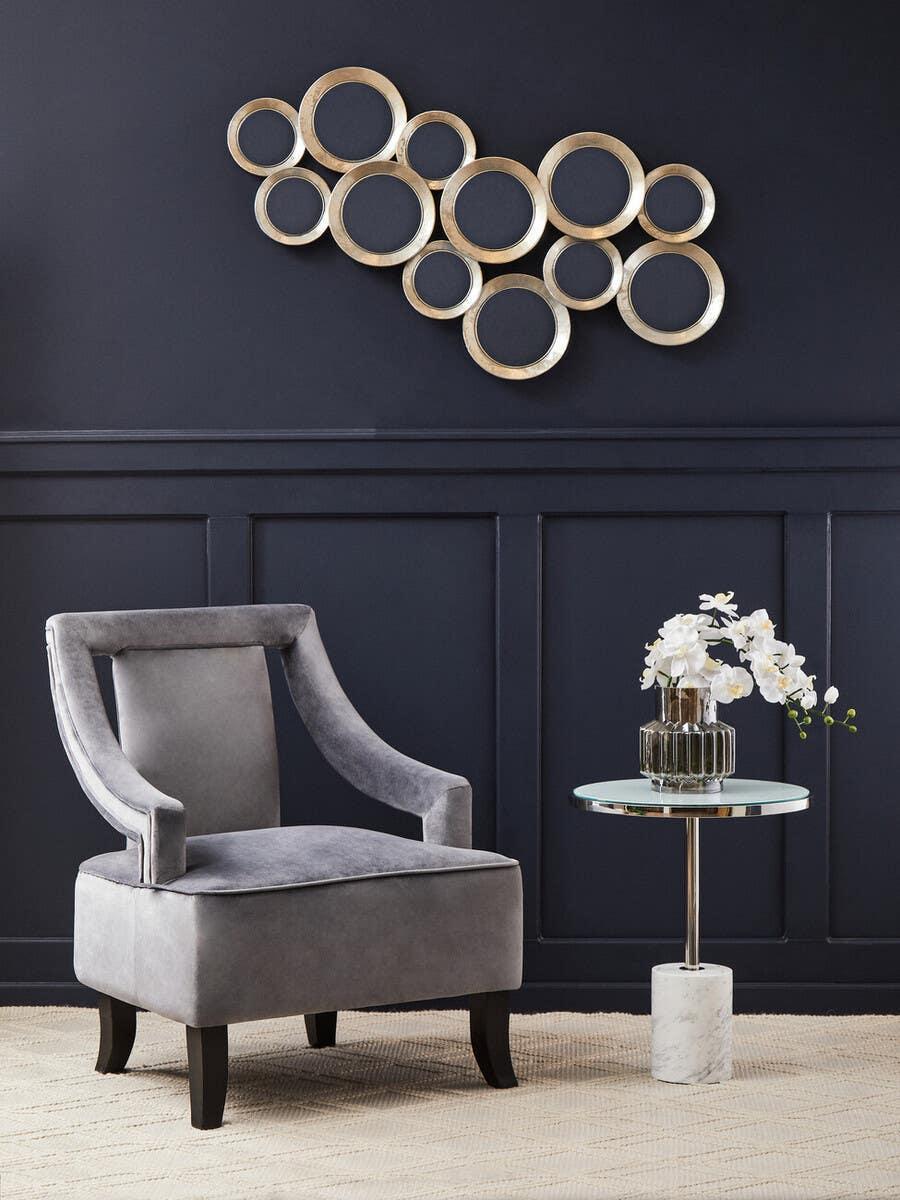 Grey accent chair beside glass side table with flowers and gold circular wall art in modern living room