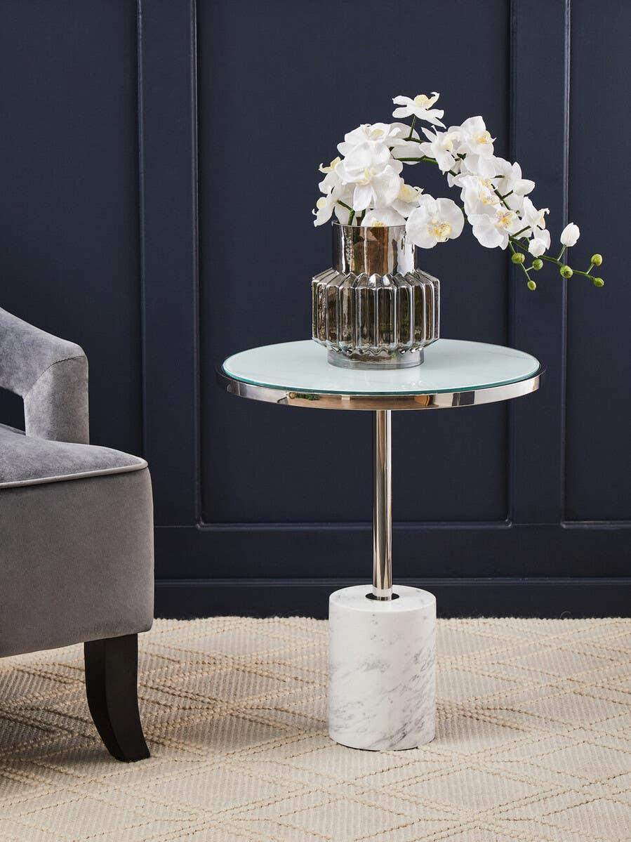Glass top side table with marble base and vase of white orchids in modern living room