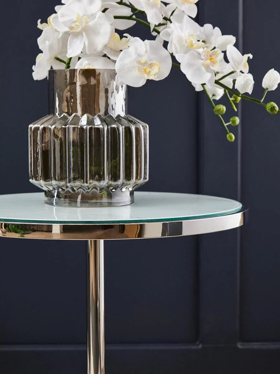 Glass side table with metal base and ribbed vase holding white orchids