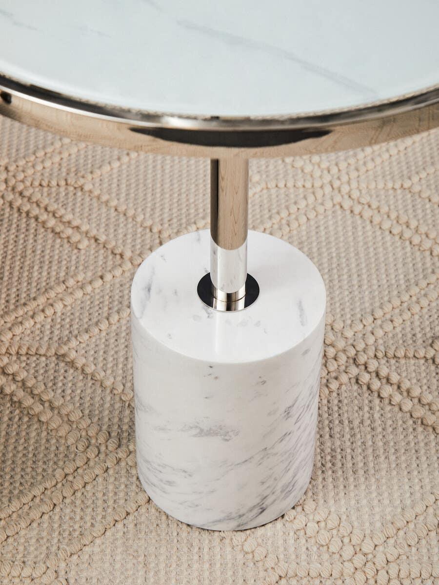 Round marble side table with chrome base on textured beige rug