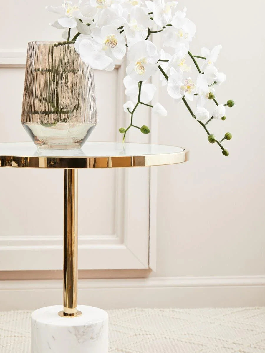 Glass side table with gold trim and marble base, ribbed vase and white orchid flowers