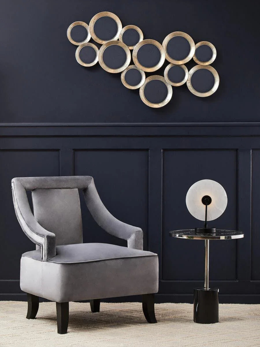 Grey velvet accent chair with black legs beside round side table and modern wall art