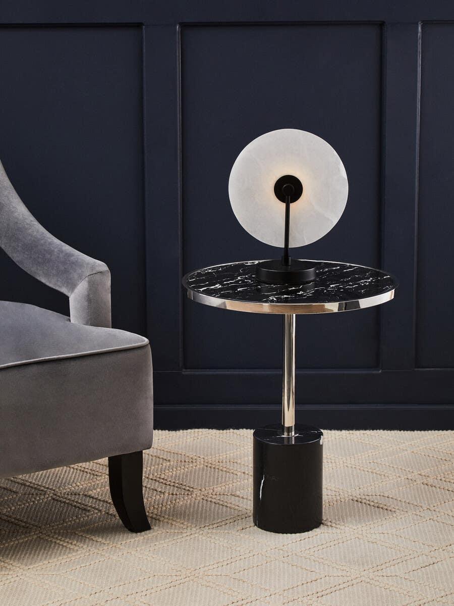 Round black marble side table with modern table lamp beside grey velvet armchair