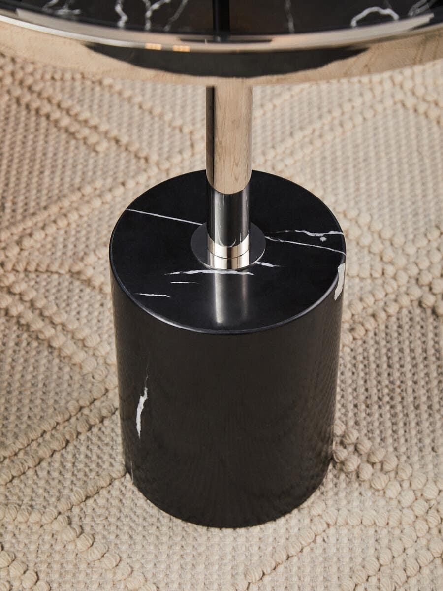 Black marble side table base with chrome pole on textured beige rug
