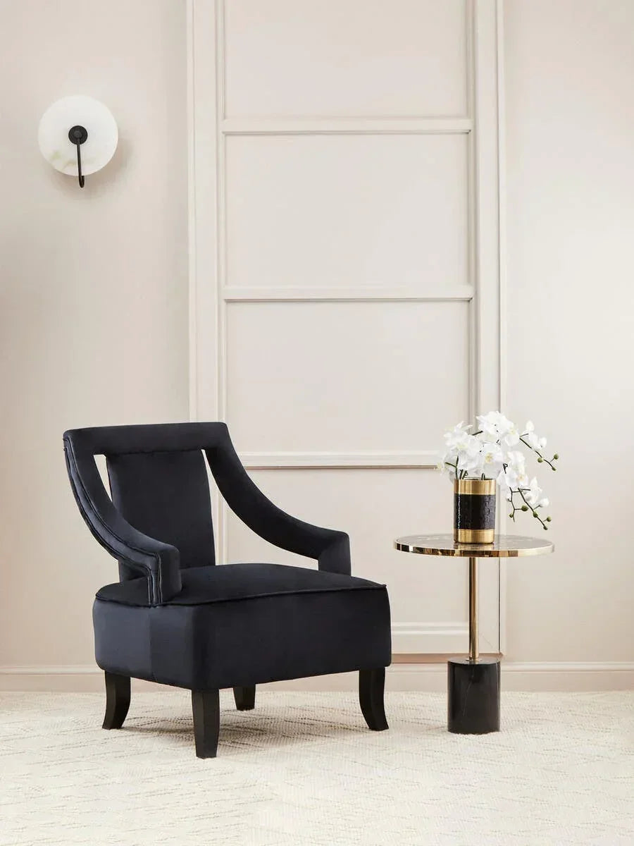 Black velvet accent chair with curved arms beside gold side table and white orchid