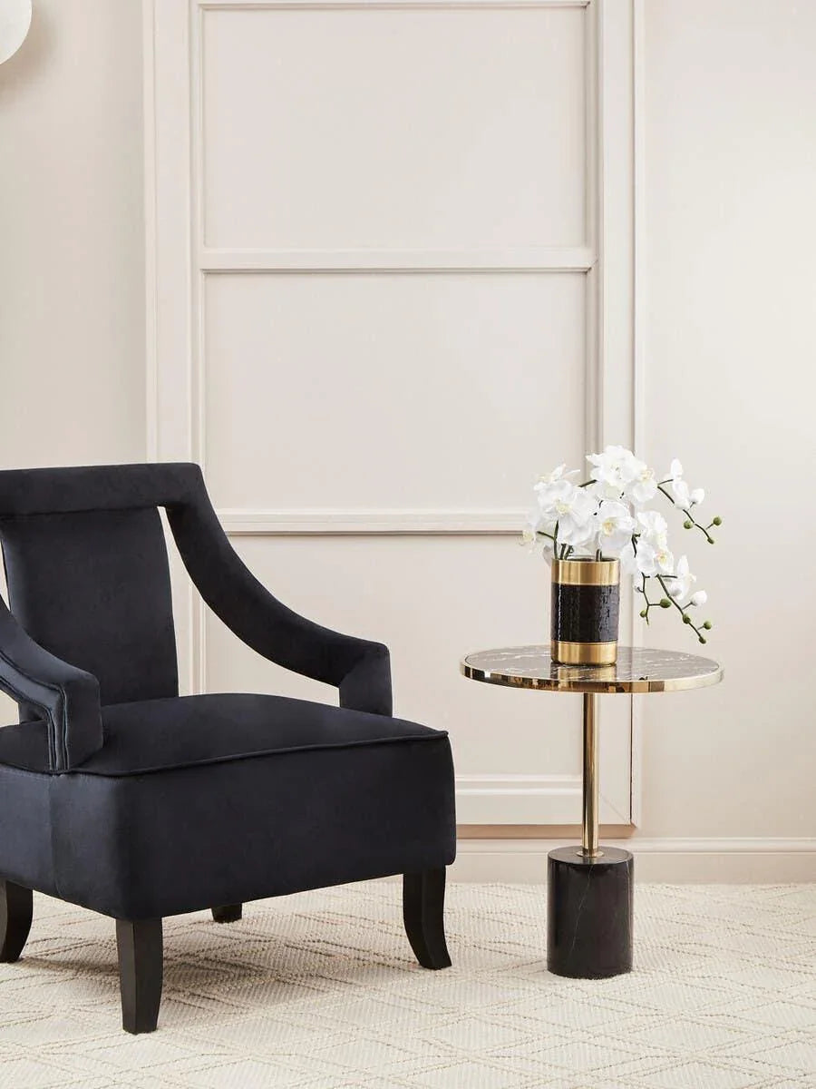 Velvet accent chair next to round marble side table with white orchid in modern living room