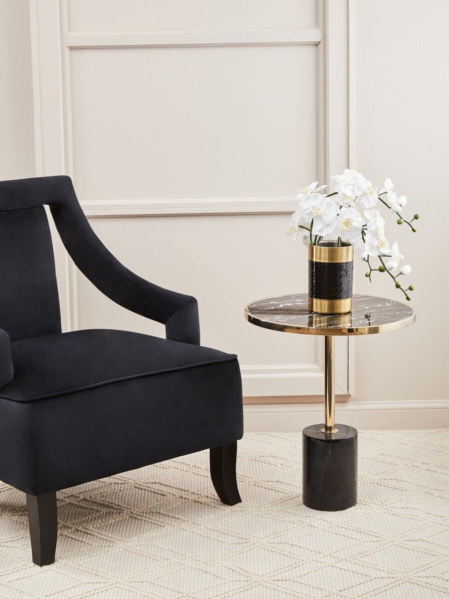 Black velvet armchair beside marble top side table with gold accent and white orchid decor