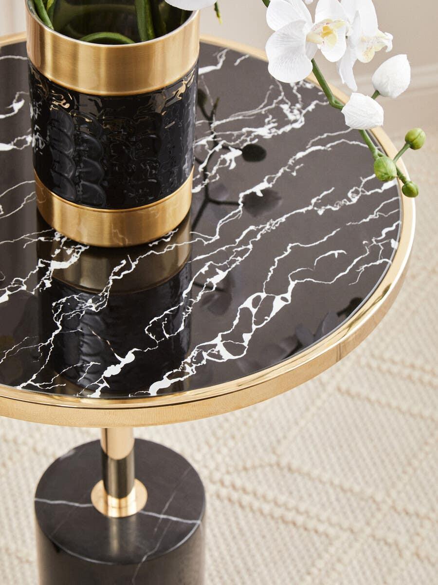 Black marble side table with gold trim and vase of white orchids