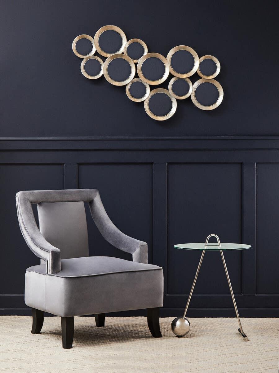 Grey velvet accent chair and glass side table against dark wall with gold circle wall art