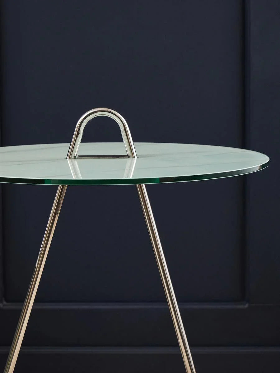 Round glass top side table with chrome handle and metal legs against dark wall