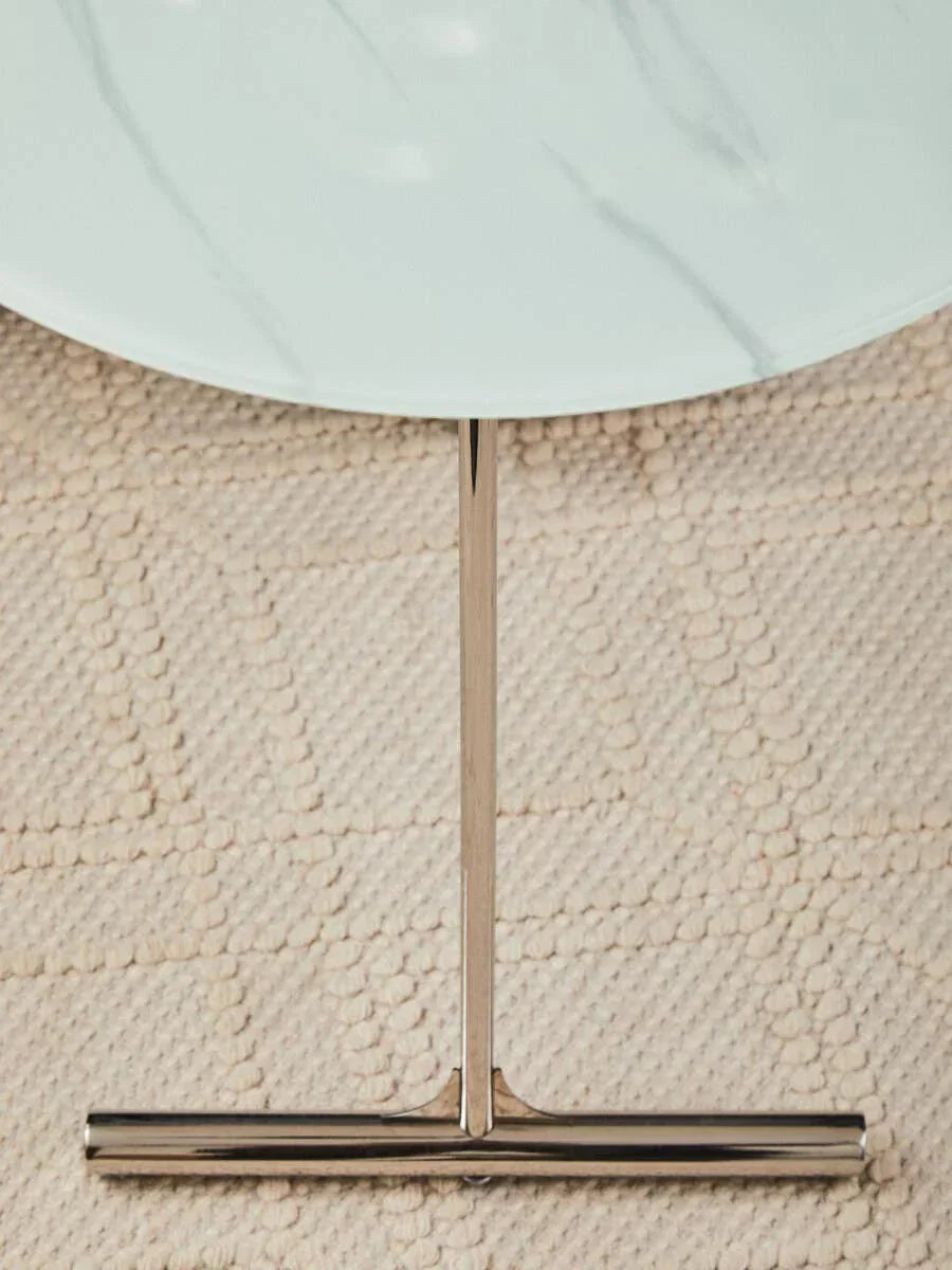 Round white marble coffee table with chrome metal base on textured beige rug