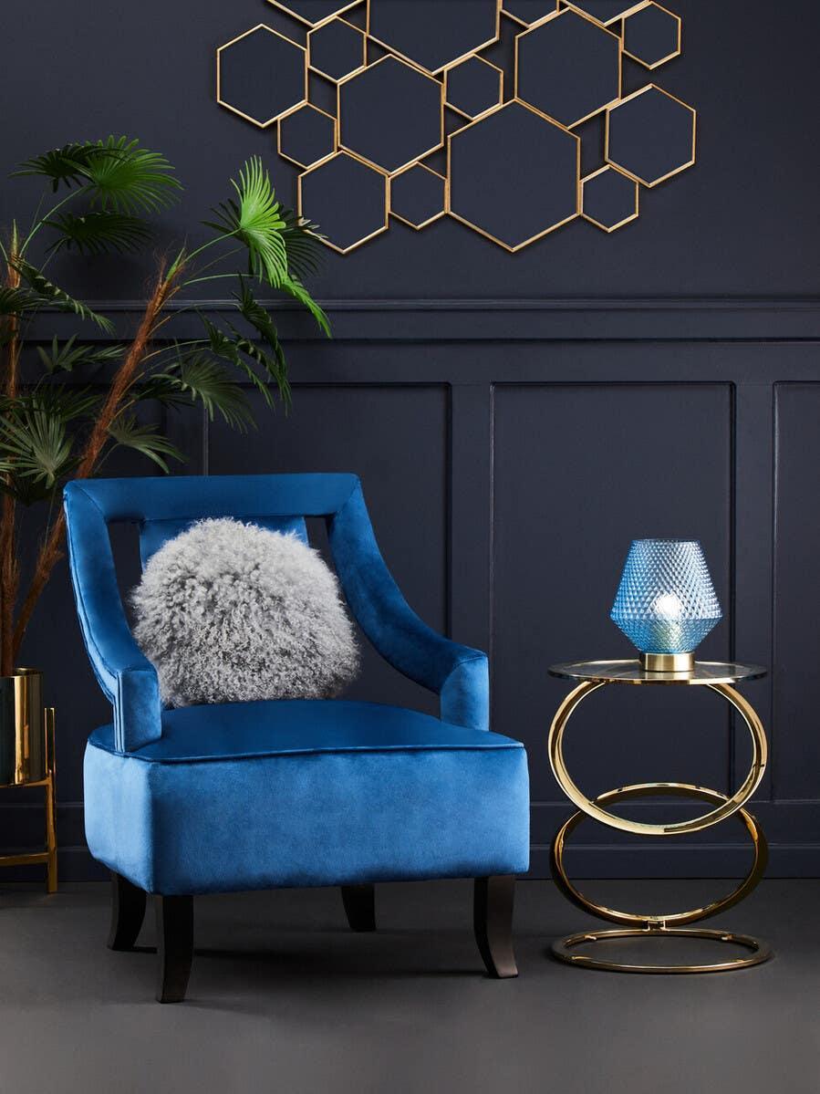Blue velvet accent chair with grey cushion beside gold glass side table in modern living room