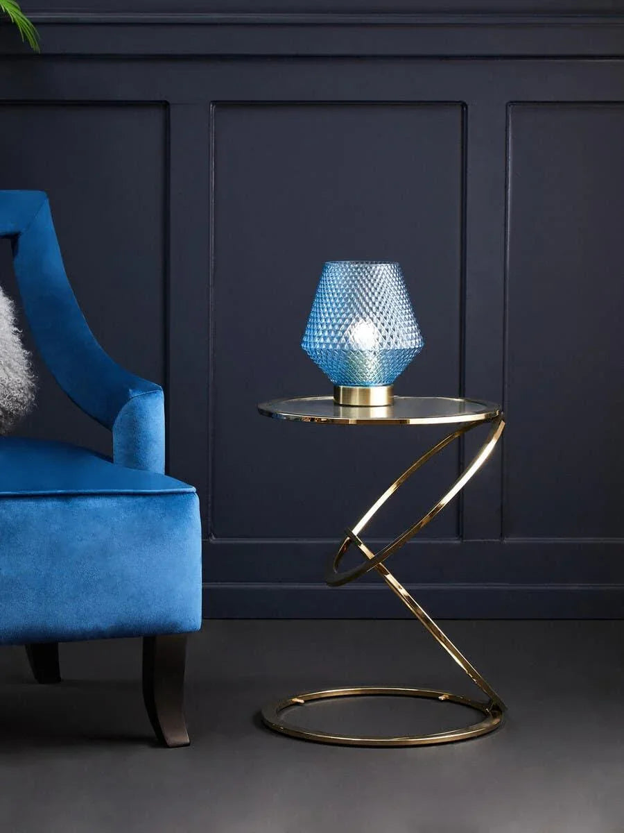 Blue accent chair next to gold metal side table with blue geometric glass lamp