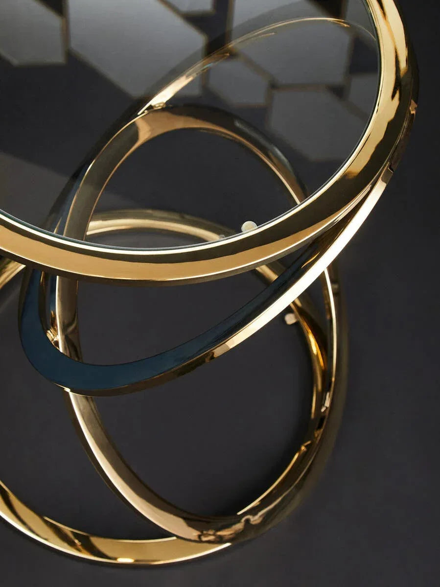 Round glass coffee table with gold metal circular base on dark surface