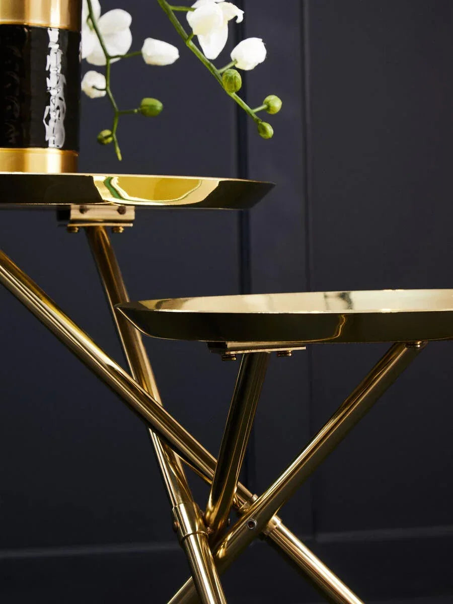 Gold metal side table with black vase and white flowers against dark wall background