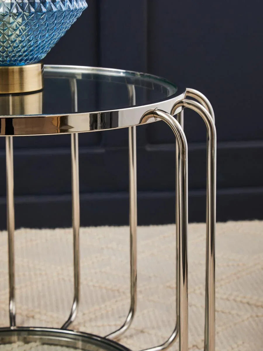 Round glass side table with chrome legs on patterned beige rug, close-up view