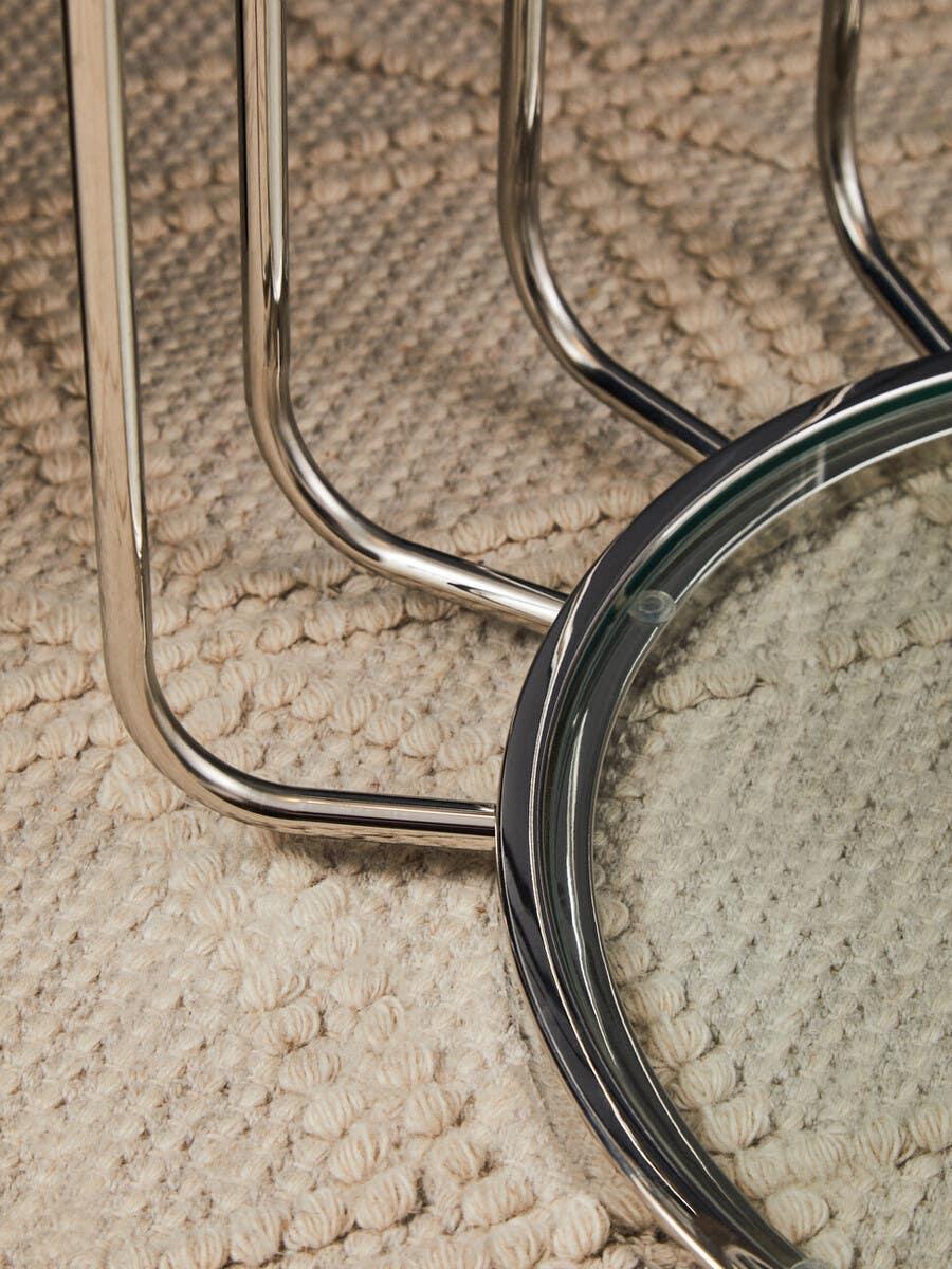 Chrome metal coffee table base with round glass top on textured beige rug