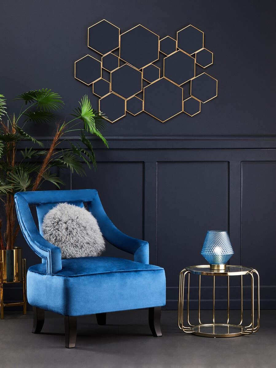 Blue velvet accent chair with grey cushion beside gold glass side table and geometric wall art