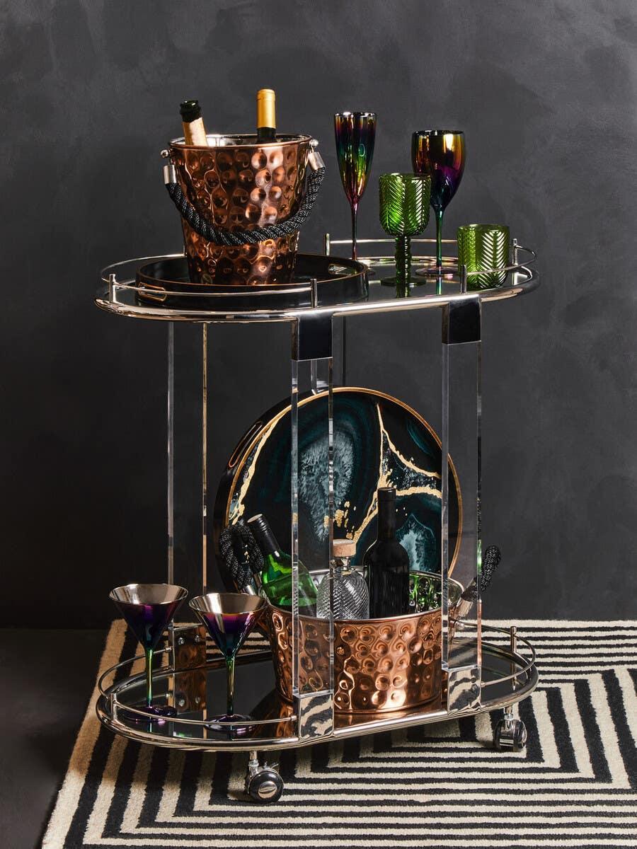 Chrome and copper drinks trolley with wine, glasses, and bar accessories on striped rug