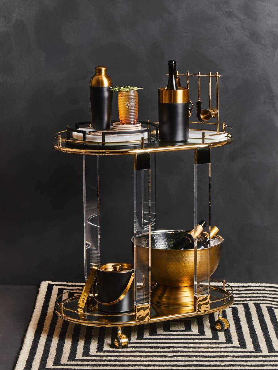 Gold and glass bar cart with black and gold barware, champagne bucket and cocktail shaker