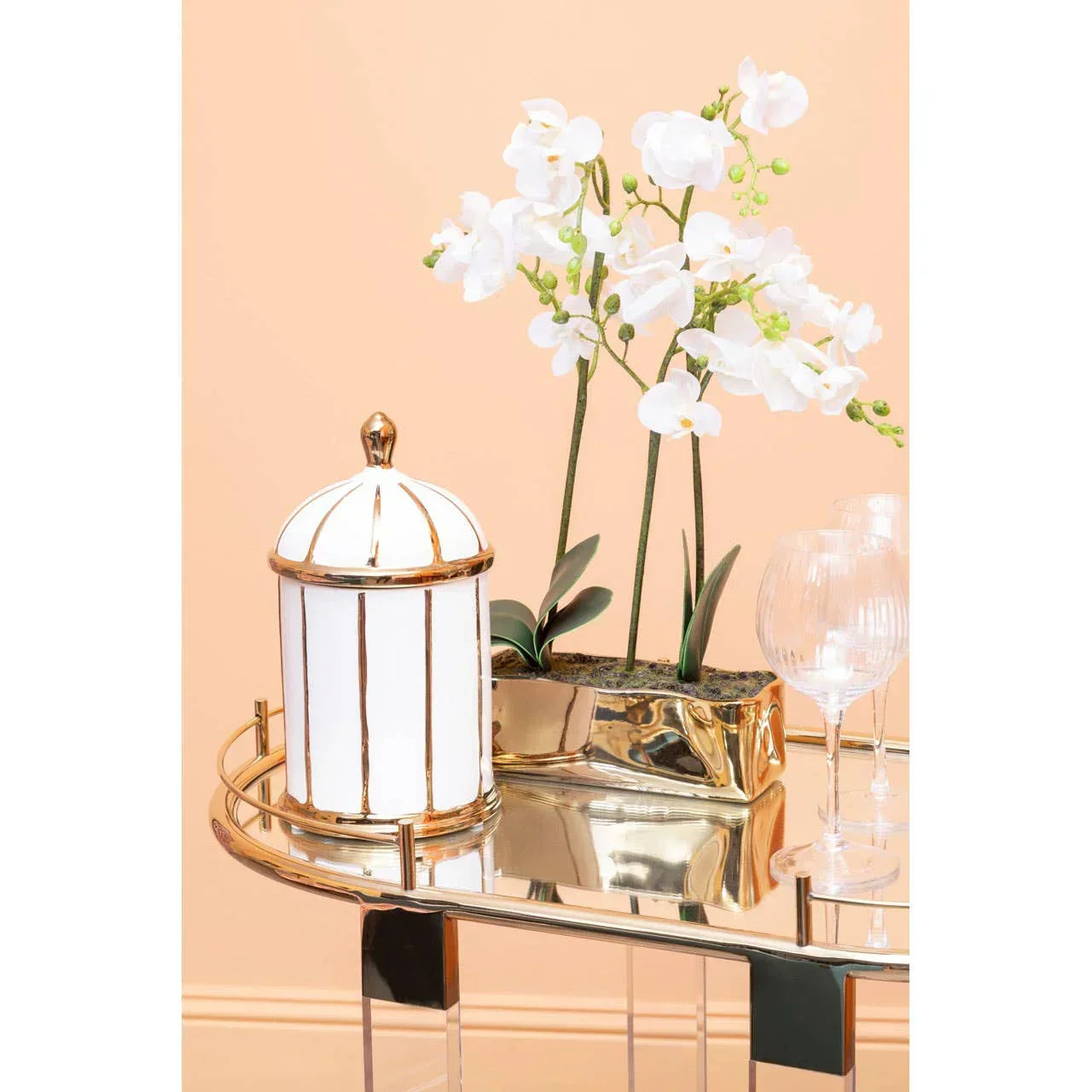 Mirrored console table with white and gold jar, glassware, and artificial orchid display