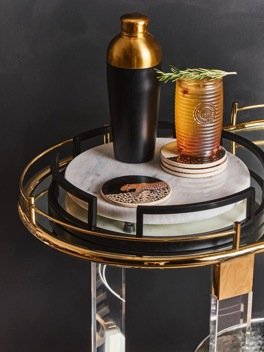 Gold and black drinks trolley with marble top, cocktail shaker, glass, and animal print coaster