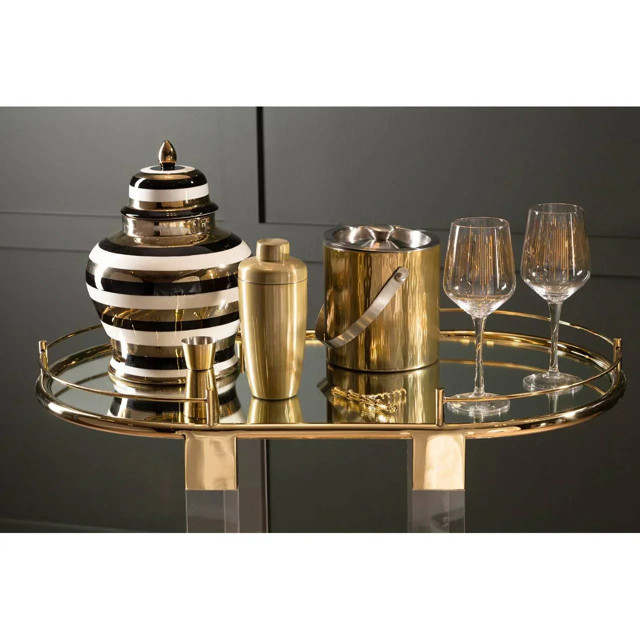 Gold drinks trolley with striped ceramic jar, cocktail shaker, ice bucket, and two wine glasses
