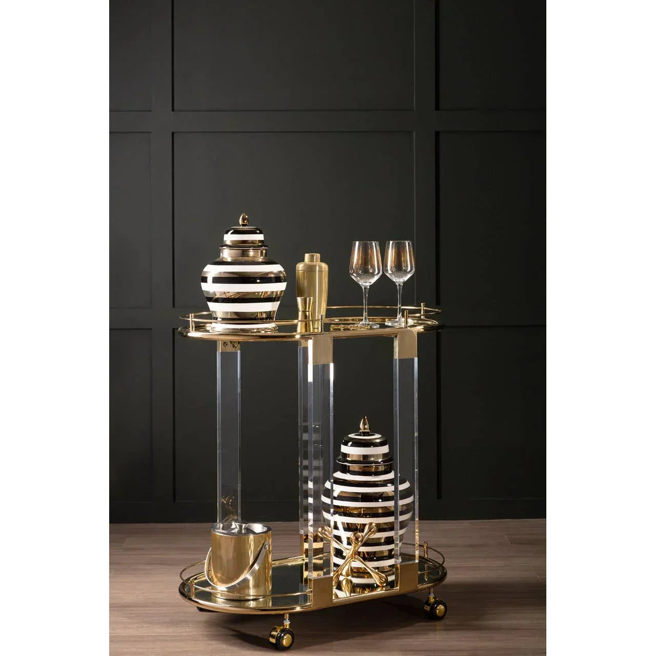 Gold and glass drinks trolley with striped jars, glasses, and bar accessories on wood floor