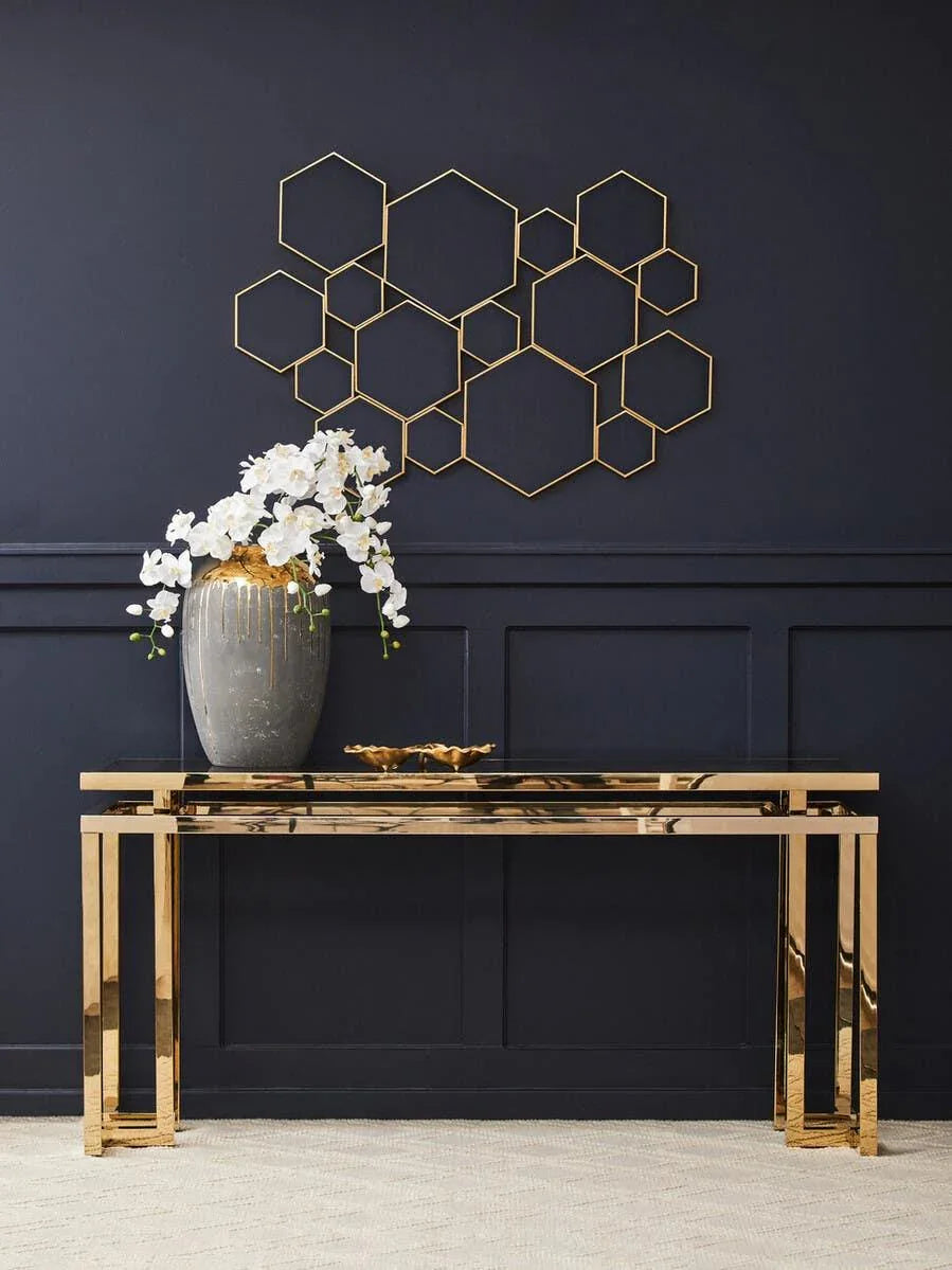 Gold console table with reflective finish and vase of white orchids against navy wall