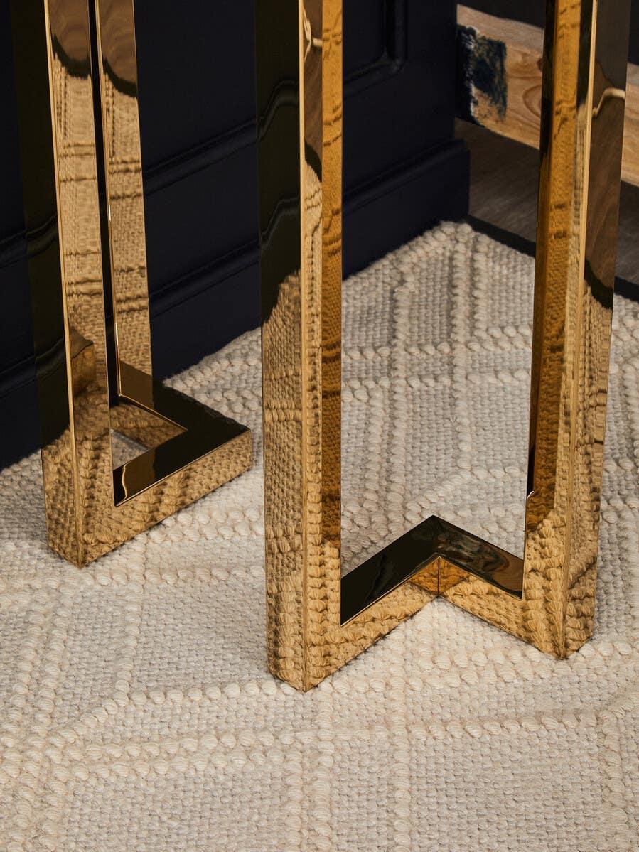 Gold metal table legs on cream textured rug in a modern interior setting