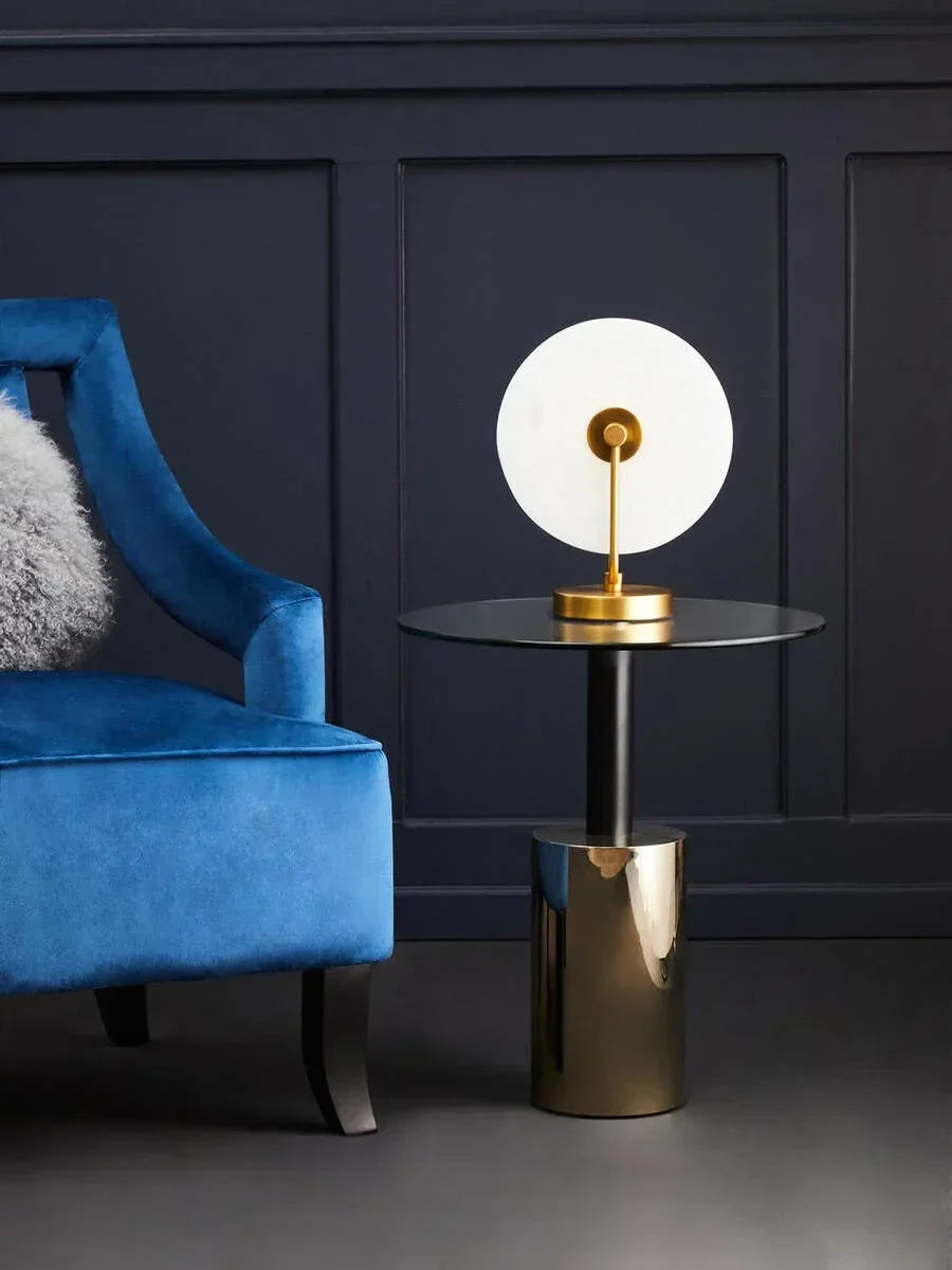 Modern black and gold side table with decorative lamp beside blue velvet accent chair