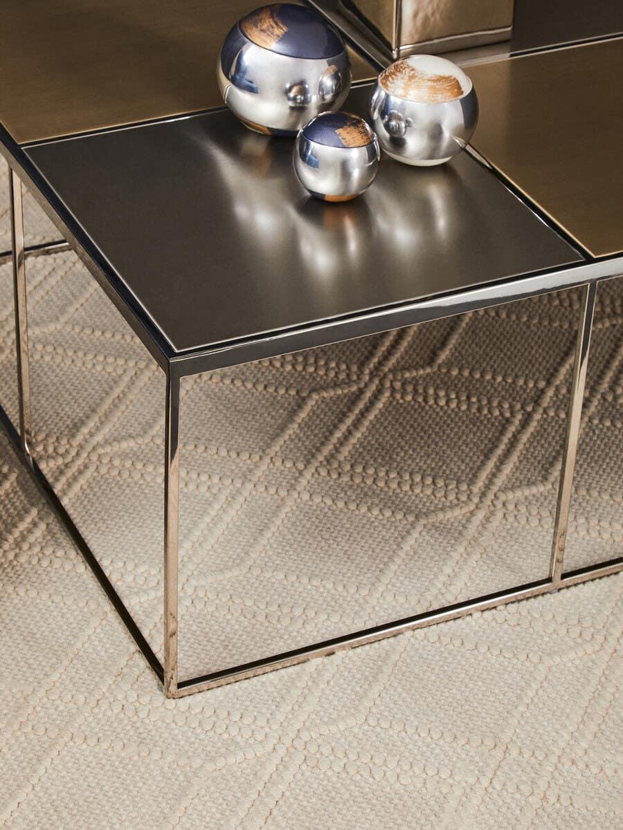 Metal coffee table with reflective top and decorative spheres on textured cream rug