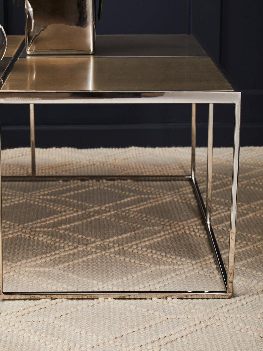 Square metal coffee table with gold top and chrome frame on beige textured rug