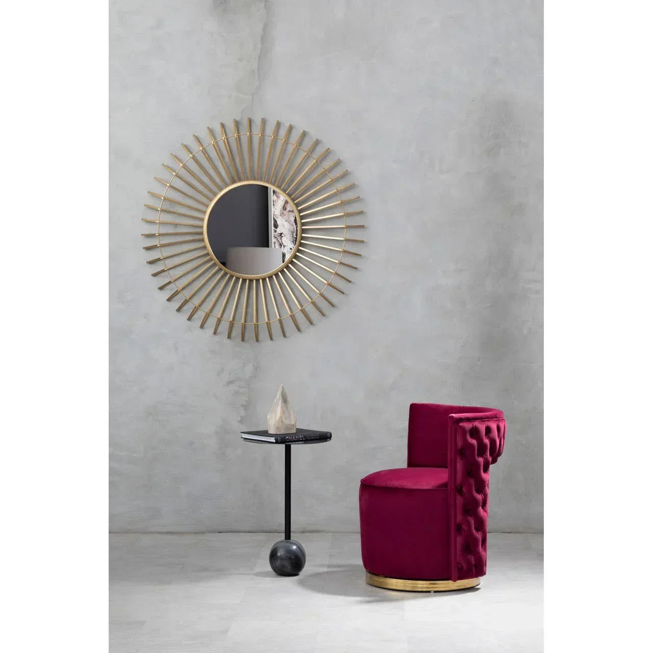 Plush velvet accent chair in deep red with gold trim beside a black round side table and sunburst wall mirror