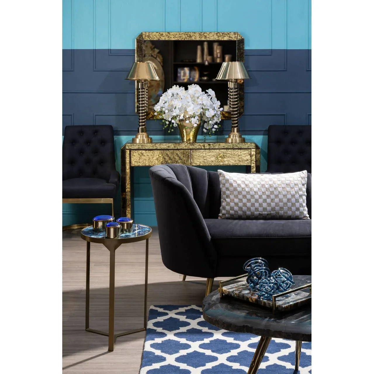 Black velvet sofa with checkered cushion, gold console table and lamps, blue accent chair