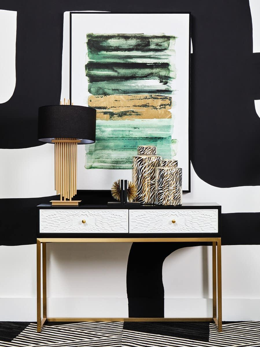 Modern console table with gold frame, black and white drawers, decor, and abstract wall art