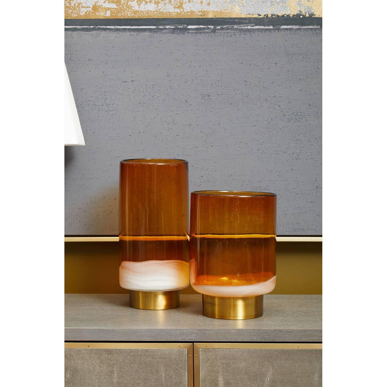 Amber glass vases with gold bases on a sideboard against a grey and gold wall