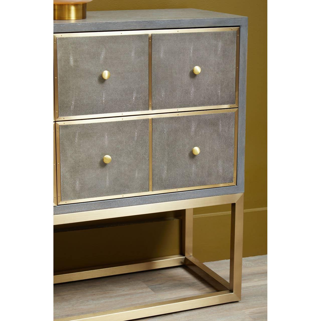 Grey and gold four drawer chest with brass knobs and metal frame on wood floor