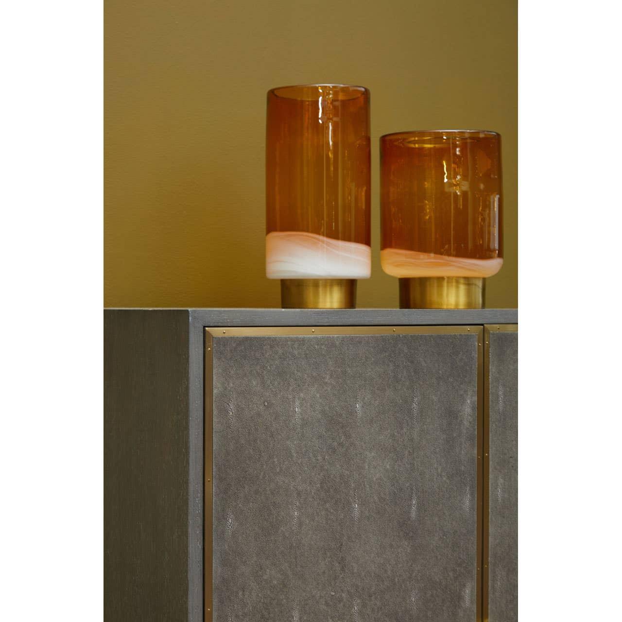 Amber glass table lamps with gold bases on a modern grey cabinet