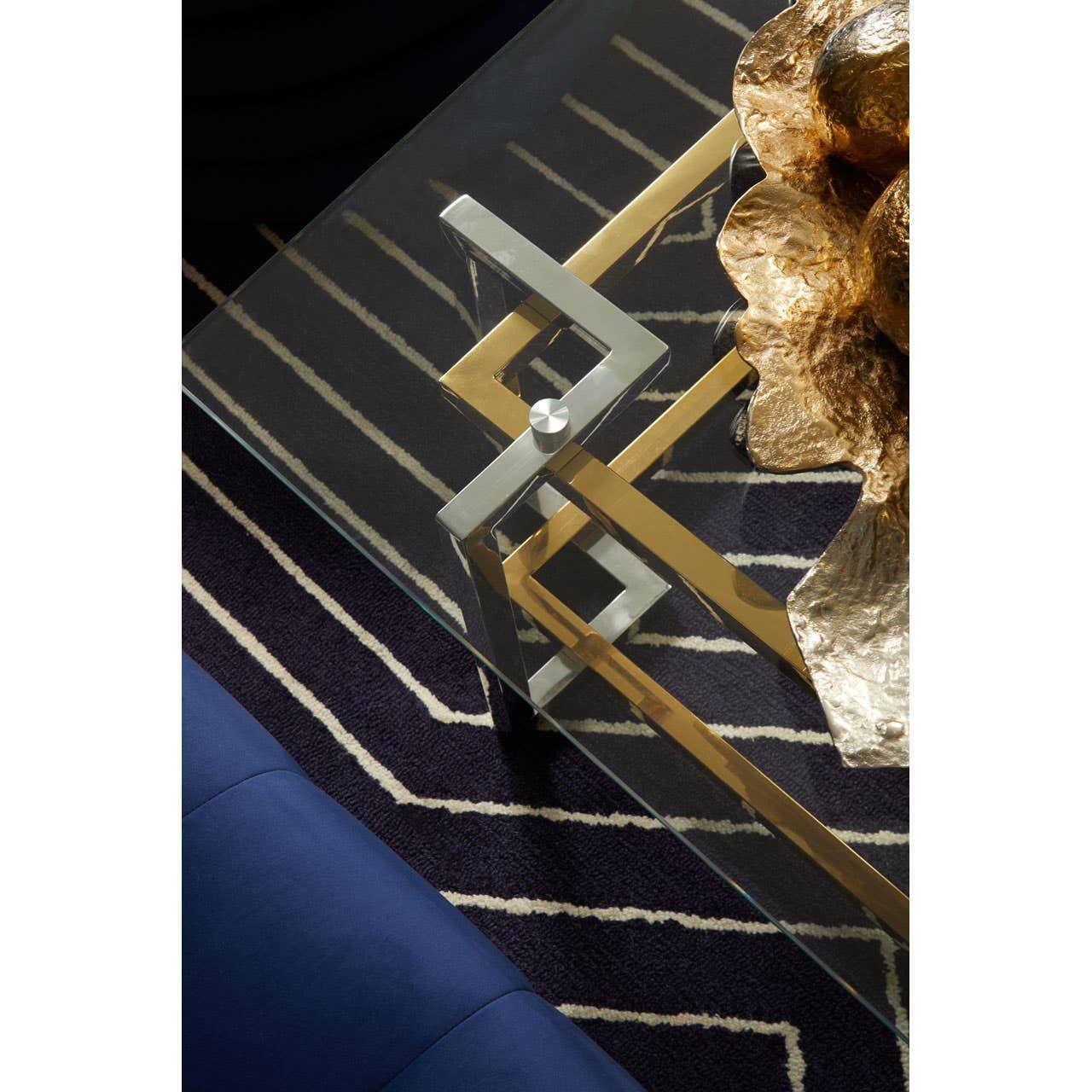 Glass coffee table with gold metal frame on striped rug, decorative gold centerpiece on top