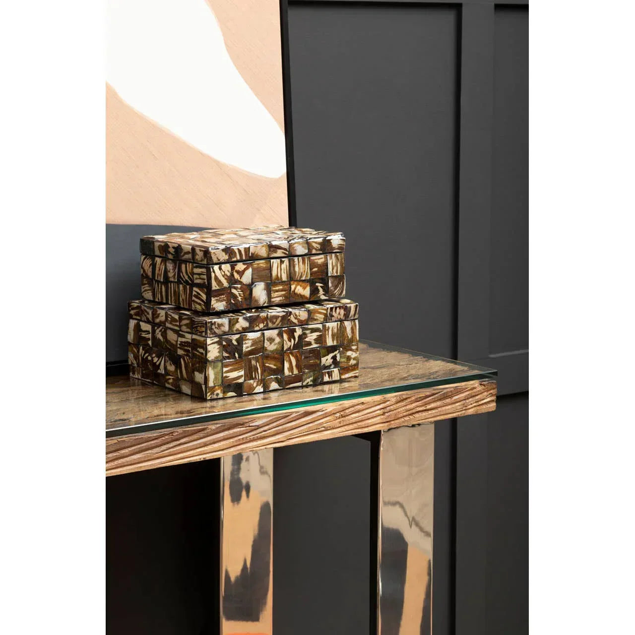 Brown mosaic storage boxes stacked on a glass console table against black panel wall
