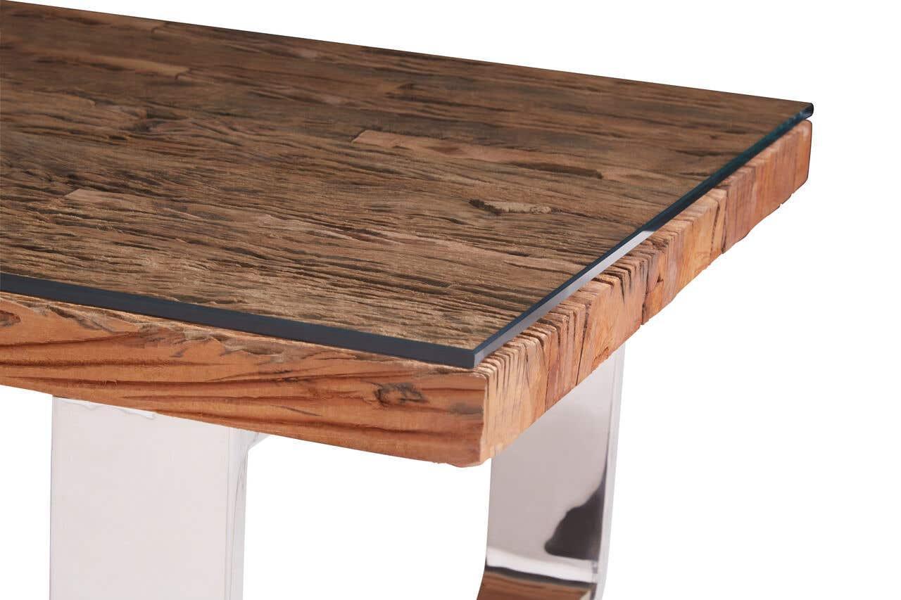 Dining table with rustic wooden top, glass surface, and chrome legs close-up
