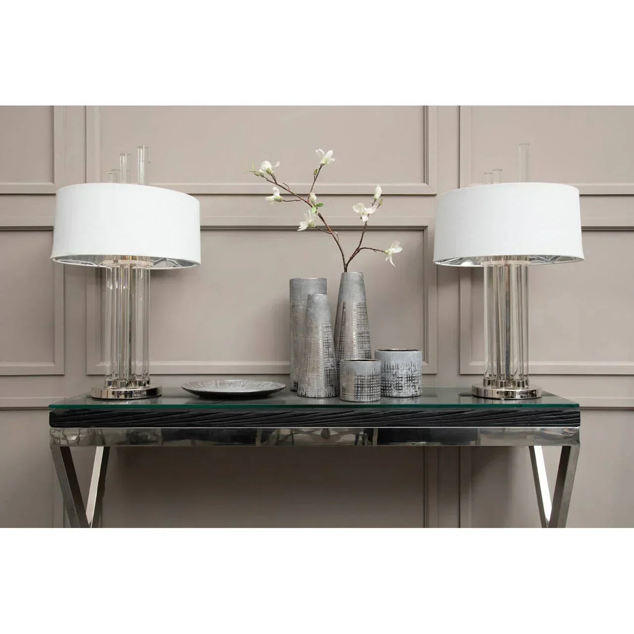 Modern glass console table with chrome legs, two white table lamps, grey vases and plate